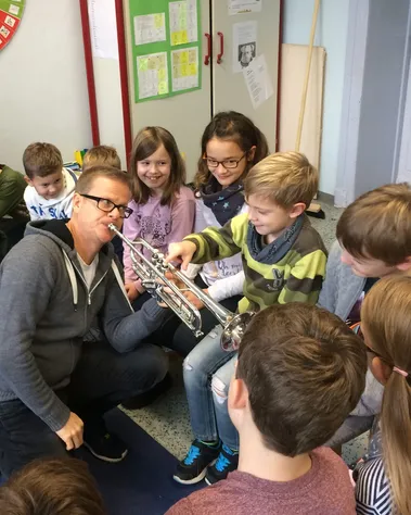 Musiker mit Trompete zeigt Kindern sein Instrument